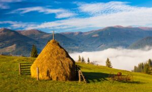 Stack of hay on a green meadow in the mountains Stack of hay on a green meadow in the mountains under a cloudy summer sky at sunrise